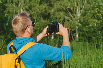 A man takes pictures with a SLR camera in the forest. Against the backdrop of beautiful greenery.