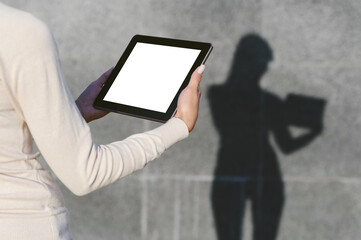 Mock-up of a tablet in the hands of a girl. Against the background of a gray concrete wall, a silhouette remains with a clear shadow.