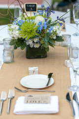 Tables set for an outdoor wedding reception in white, with blue flowers as decor