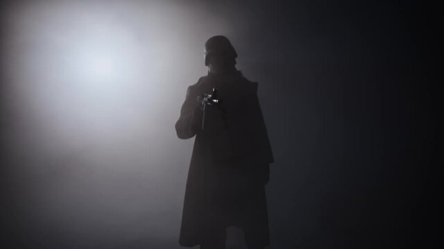 Soldier in trenchcoat takes aim at into camera with rifle, dramatic silhouette
