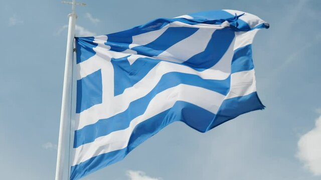 Slow motion of Greek flag rippling on the wind against blue sky.