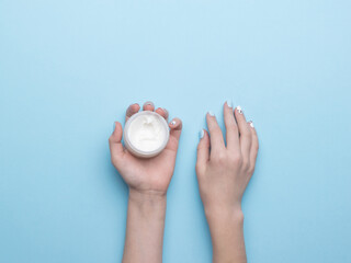 Women's hands with a jar of hand cream on a blue background. Flat lay.