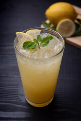 glass of iced lemonade with fresh lemon and mint by lemon reamer on wood