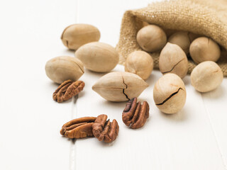 Peeled and unpeeled pecans are spilled out of a bag on a white table.