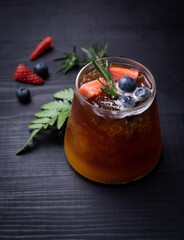 glass of iced americano black coffee and layer of orange with rosemary,blueberries,orange and strawberry on wood