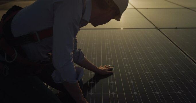 Cinematic shot of assistance technical worker in uniform checking operation and efficiency of photovoltaic solar panels on roof at sunset. Concept: sustainable renewable green, bio eco clean energy.