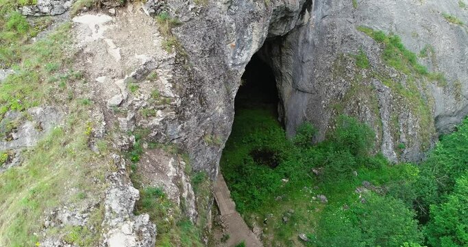Kapova cave in Nature Reserve Shulgan-Tash. The entrance is huge arch with river flows out of ground. Limestone karst cave in the Burzyansky District of Bashkortostan. Aerial drone view at summer day
