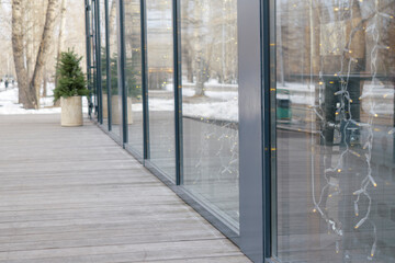 Glass shop window with yellow garland bulbs. Wooden flooring. Christmas tree, snow. View is an...