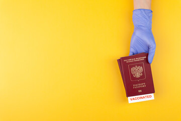 Hand in medical glove holding passport with vaccinated stamp on yellow background