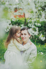 Happy mother's day. Little girl hugs her mother in the spring cherry garden. Portrait of happy mother and daughter among white flowers trees. Family values. Motherhood. Mom and child in blooming park.