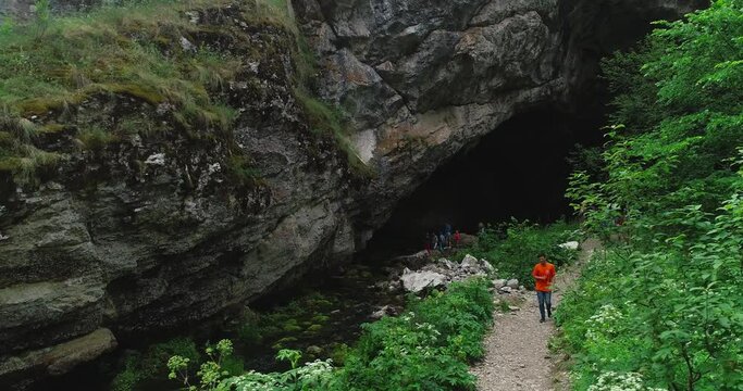 Kapova cave in Nature Reserve Shulgan-Tash. The entrance is huge arch with river flows out of ground. Limestone karst cave in the Burzyansky District of Bashkortostan. Aerial drone view at summer day