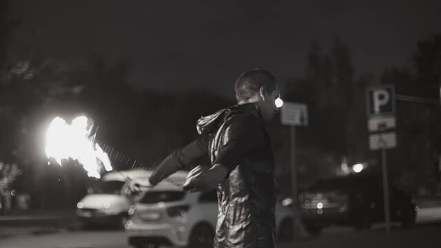Black and white footage of a guy performing at a fire show at night on a sidewalk in the city. Shooting in slow motion