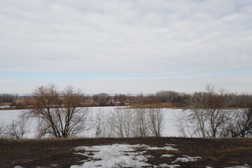 Rural area in early spring. In the foreground, a river under the snow.