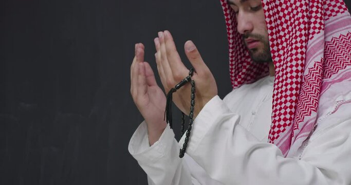Middle eastern Arabian man in traditional clothes in front of black chalkboard praying 