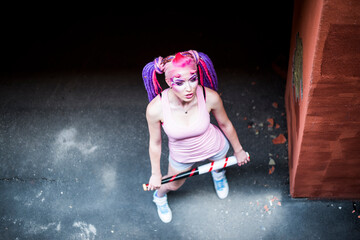 Aggressive pink punk woman posing with a baseball bat. Up view. Young candy demon girl have red...