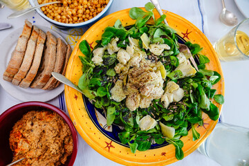 A tabletop view of a large watercress salad with artichoke hearts and hummus on the side.
