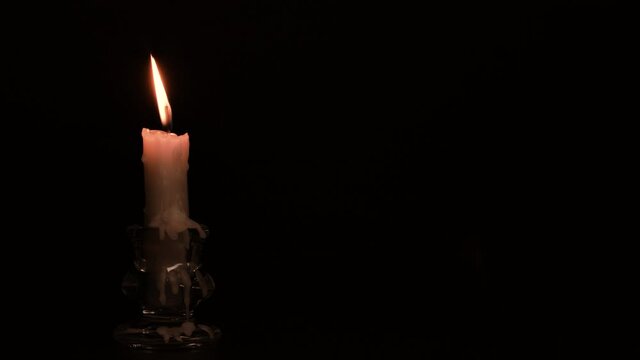 Close-up burning single candle flame isolated on black background, 4K video