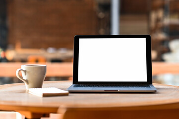 Fototapeta premium Mockup blank screen laptop with coffee and notebook on the table, Taken from the front.