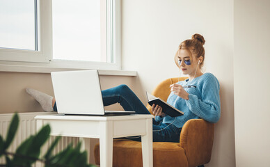 Caucasian student with eye patches is reading a book and using a laptop at home during spa...
