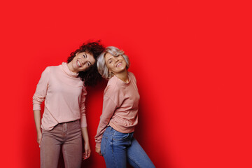 Lovely cheerful caucasian sisters with curly hair are smiling on a red studio wall with free space advertising something