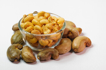Cashew nuts in clear glass cup and unpeeled cashews on white background