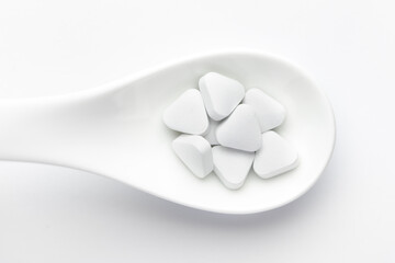 Macro Close up of medicinal or herbal white pill on a white ceramic spoon. Top view, white background.