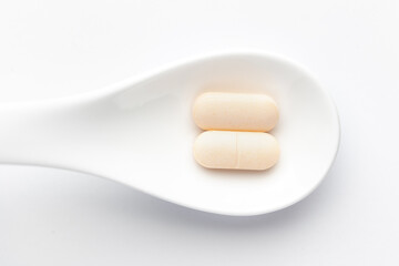 Macro Close up of medicinal or herbal pale yellow tablet on a white ceramic spoon. Top view, white background.