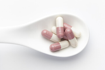 Macro Close up of medicinal or herbal white-brown capsule on a white ceramic spoon. Top view, white background.
