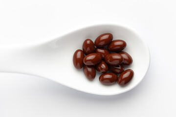 Macro Close up of medicinal or herbal dark red-brown pill on a white ceramic spoon. Top view, white background.