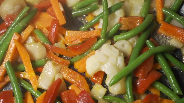 Cocking green and colorful fresh vegetables in iron pan, stewed vegetables. Homemade vegan dish with veggies, asian cuisine. Preparing dinner with carrots, broccoli. Smoke evaporation in the kitchen