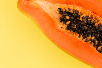 Half ripe papaya fruit with seeds on yellow background, copy space, flat lay