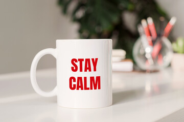 Coffee mug with text - STAY CALM in workplace background.