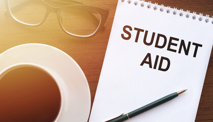 STUDENT AID - text on paper with cup of coffee and glasses on wooden background in sinlight.