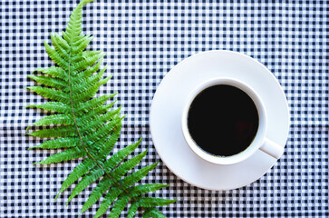 Flat lay of black coffee in white ceramic cup on classic black tablecloth  with green fern leaves 