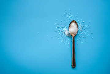 Flat lay of white sugar in wooden spoon on blue background with copy space 