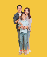 Happy Asian young family with one child standing embracing and smiling at camera isolated on yellow