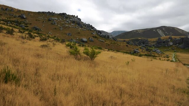 Pan shot of yellow grass field and famous Castle Hill Mountains in background with dramatic dark cloudscape at sky. Castle Hill,New Zealand.