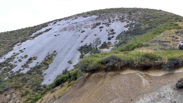Panning shot of green and sandy mountains against bright sky in Castle Hill National Park, New Zealand.
