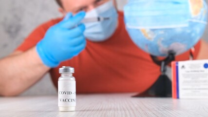 vial with a vaccine against the coronavirus, in the background a man is vaccinating the planet, the globe. Corona virus treatment concept, injection during a pandemic. Travel concept during a pandemic