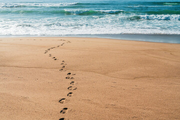 Wide sandy beach and foot prints on sand, turquoise colored sea waves on background. Sunny day, copy space