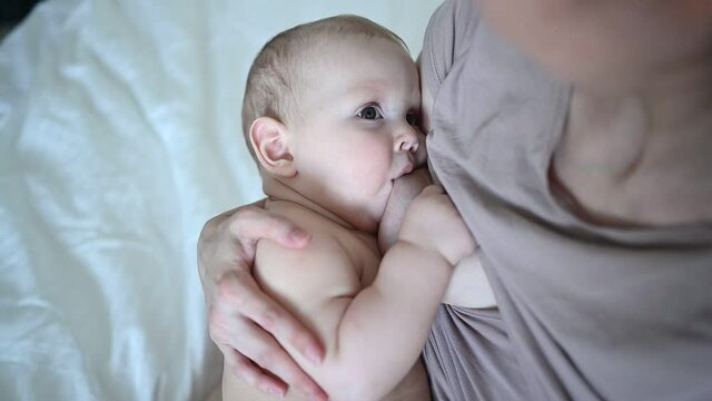 Young mother with newborn cute infant naked baby boy on the bed, holding him on arms, hugging and breastfeeds with breast milk. Healthy child, concept of hospital and happy motherhood. Nursery.