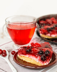 a piece of summer berry pie with a cup of red hibiscus tea, a cake decorated with strawberries and black currants in jelly, healthy nutrition, vegan dessert