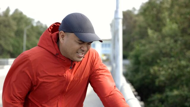 Young asian man runner jogging on the road. He take a breath tired have heart disease, asthma. Athlete resting exhausted after intense running workout.