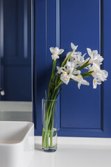 a bouquet of white daffodils in a transparent vase next to the sink against the blue wall