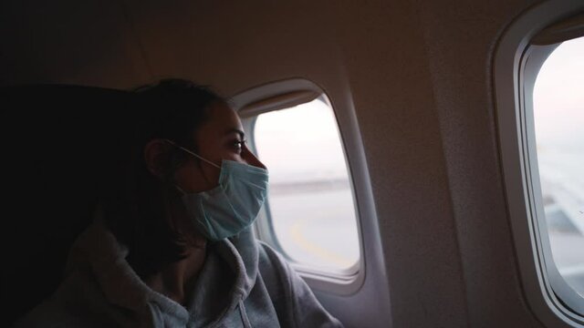 woman in hoodie and medical mask in airplane cabin. travel and air flights during Covid-19 pandemic and quarantine. new life and norms in post pandemic world