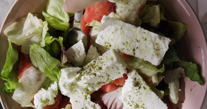 Top view of traditional Greek salad with green olives, feta cheese, tomatoes and fresh greens, taking salad with fork, Mediterranean cuisine concept.