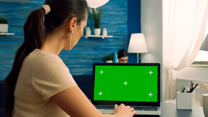 Woman typing on computer laptop with mock up green screen chroma key display working on commerce...