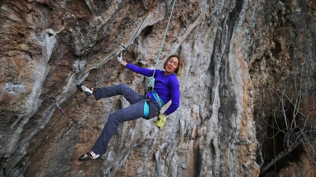 slow motion smiling tired woman rock climber hanging on rope on hard challenge route on overhanging cliff. woman resting, chalking hands and looking how to climb further
