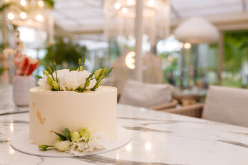 Soft focused shot of beautiful white wedding or birthday cake with roses flowers on marble table, restaurant background. Festive event sweet bakery