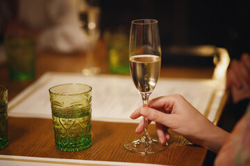 A girl with gentle manicure holds a glass of champagne in a restaurant at a table in the evening. Dinner for two in a cafe. Hand without face close up